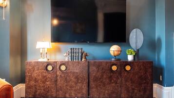 A modern living room with a dark blue wall, a flat-screen TV mounted above a brown marble console, a lamp, decorative books, a globe, and a potted plant.
