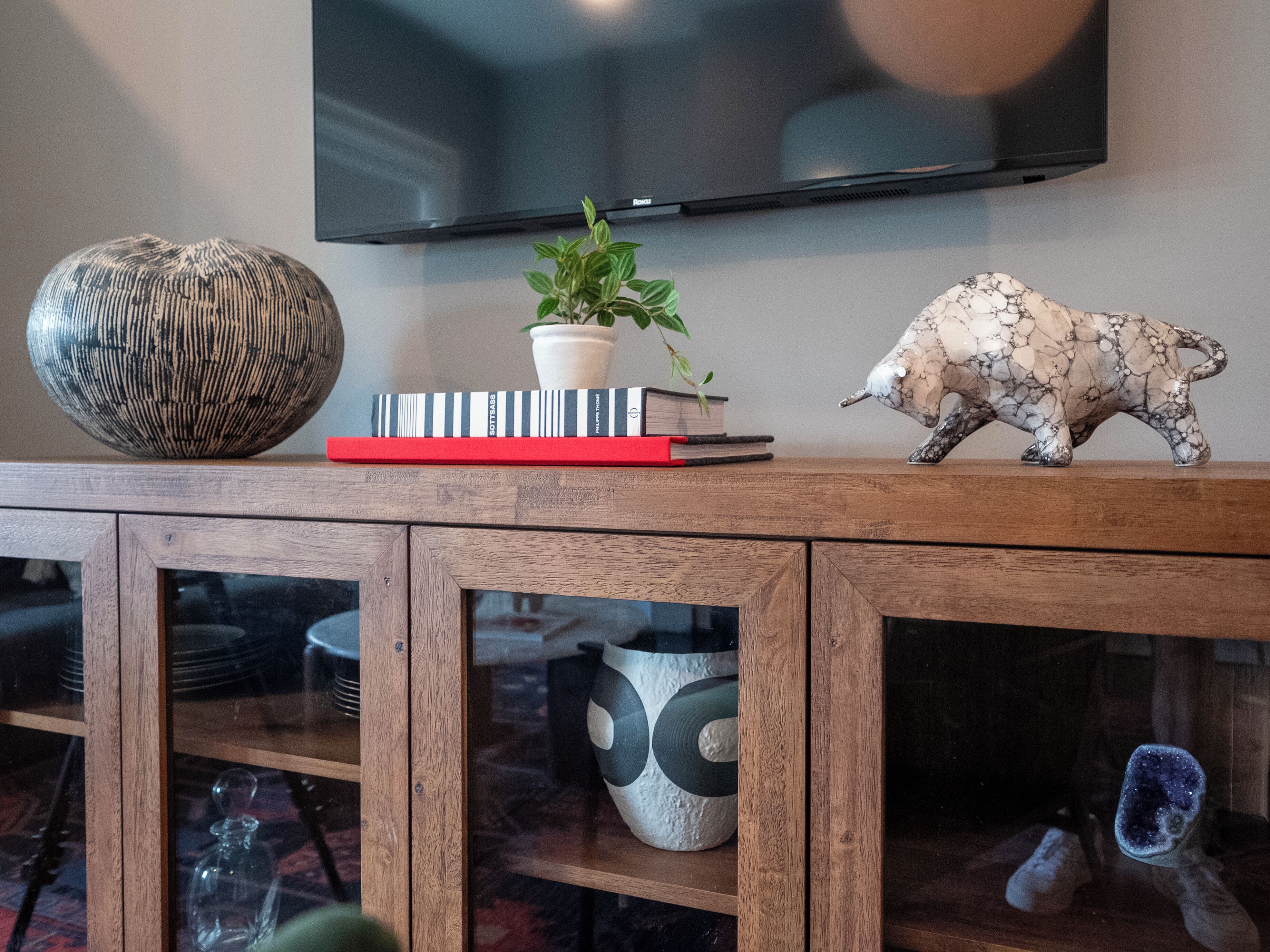 A wooden console table with decorative items, including a vase, books, a potted plant, and a bull figurine.