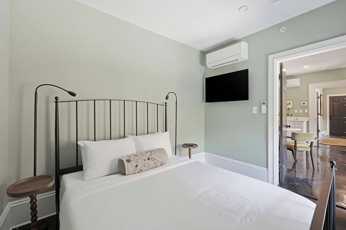 Un dormitorio con cama, mesitas de noche, televisor montado y aire acondicionado.