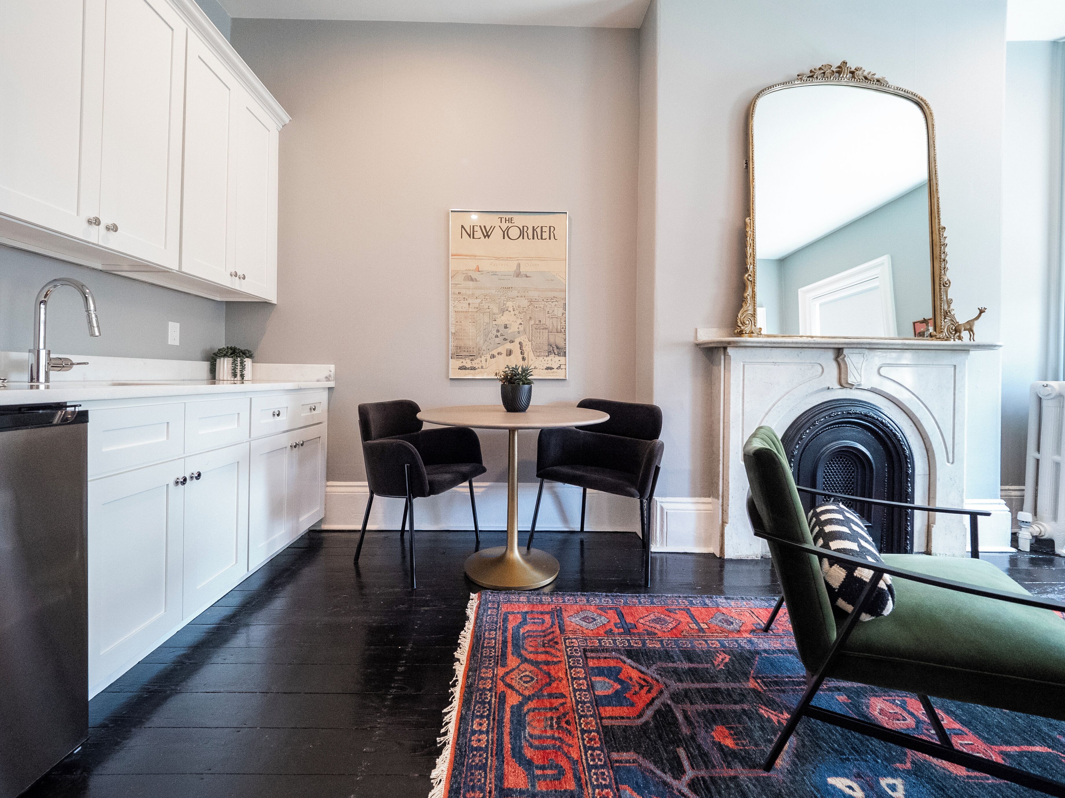 A modern kitchen with white cabinets, a dining area with a round table and two chairs, a fireplace, and a large mirror.