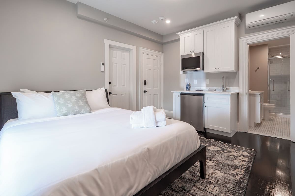 Un dormitorio moderno con una cama grande, un pequeño rincón de cocina y un vestidor.
