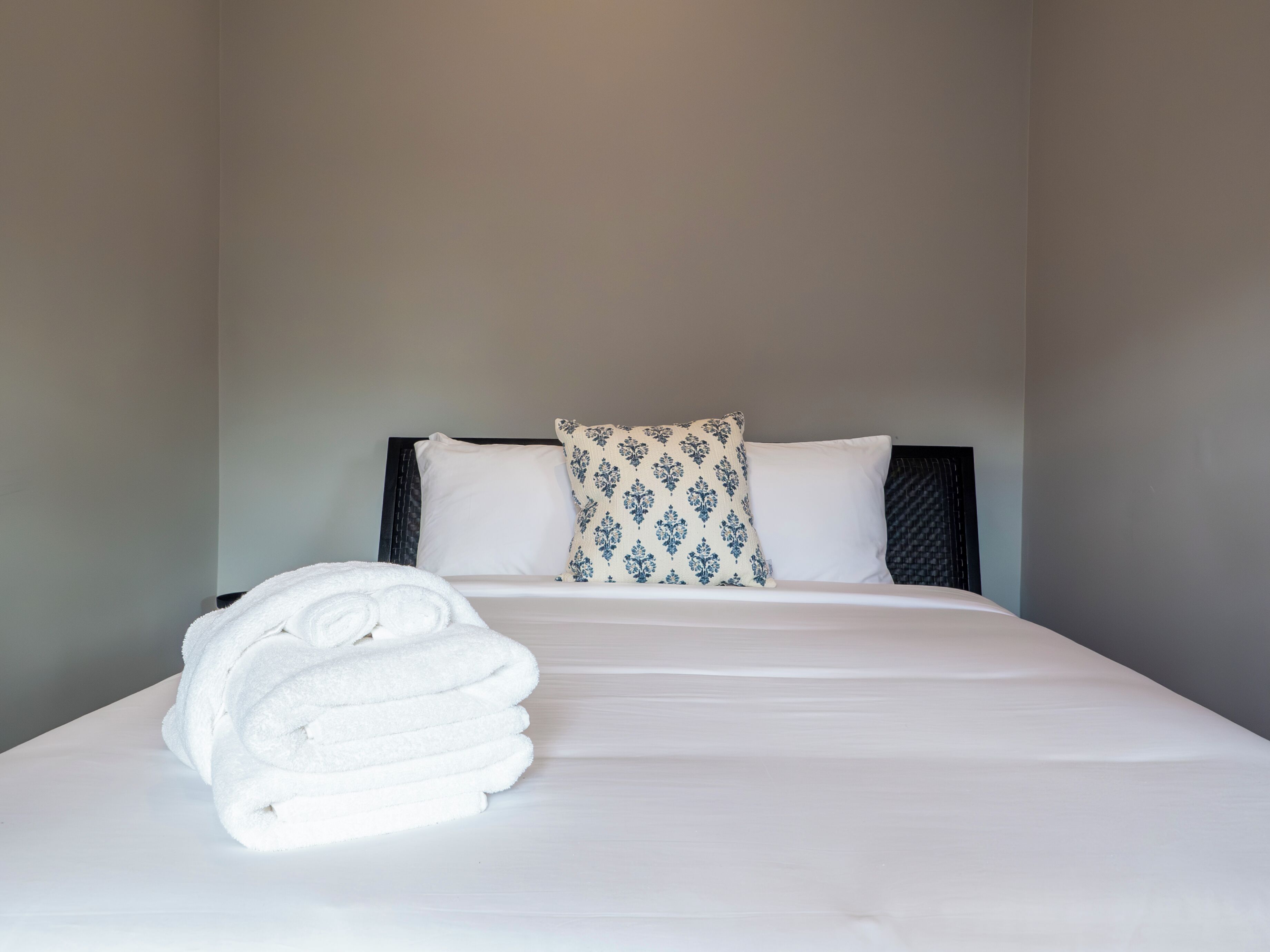 A neatly made bed with white linens and a rolled white towel on the side.