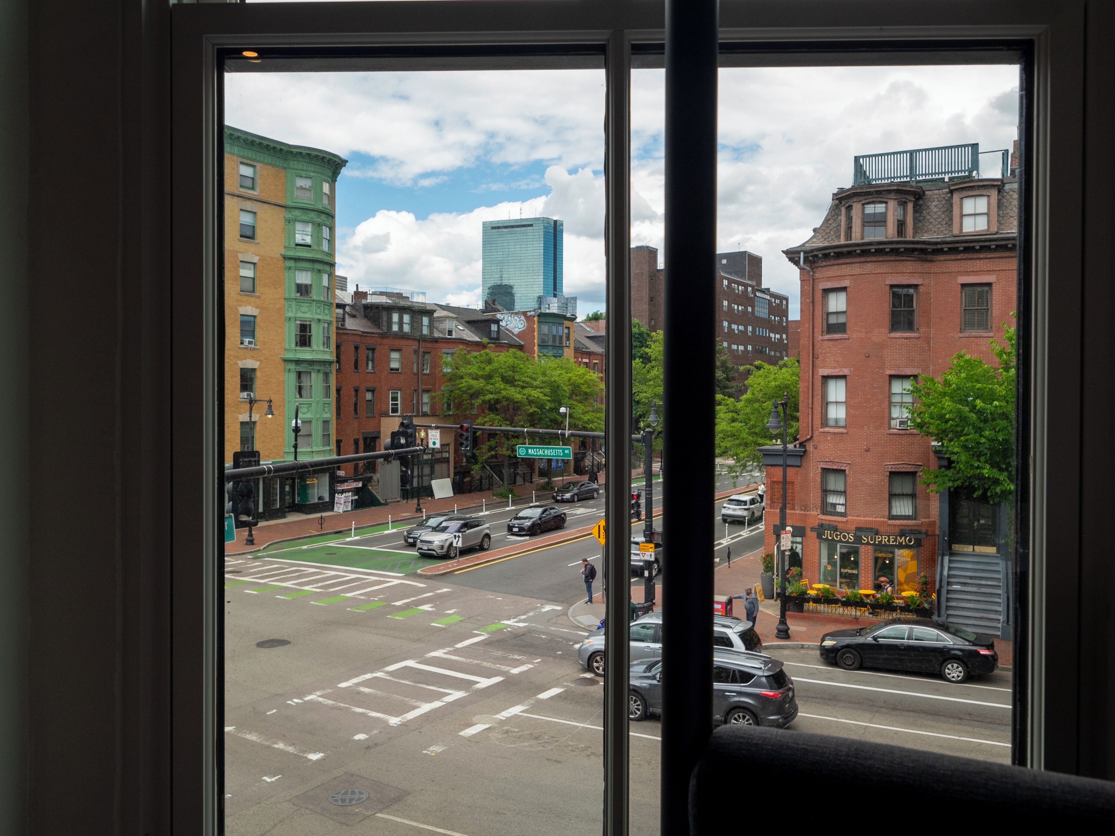 Vista de una calle urbana desde una ventana, con edificios, automóviles y un paso de peatones.