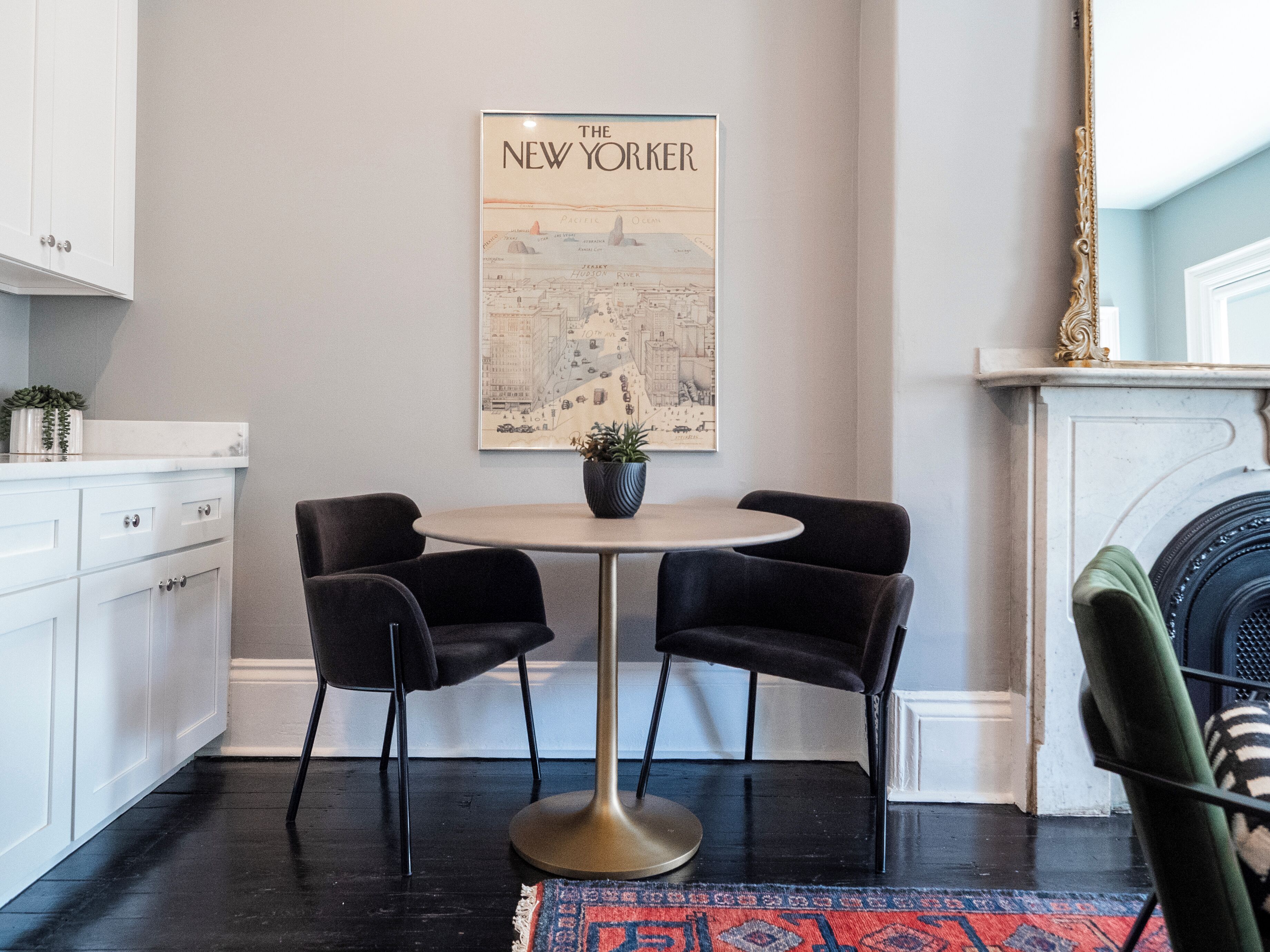 Eine moderne Küche mit weißen Schränken, einem runden Tisch mit zwei Stühlen, einer Karte von New York an der Wand und einem grünen Sessel.