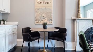 Eine moderne Küche mit weißen Schränken, einem runden Tisch mit zwei Stühlen, einer Karte von New York an der Wand und einem grünen Sessel.