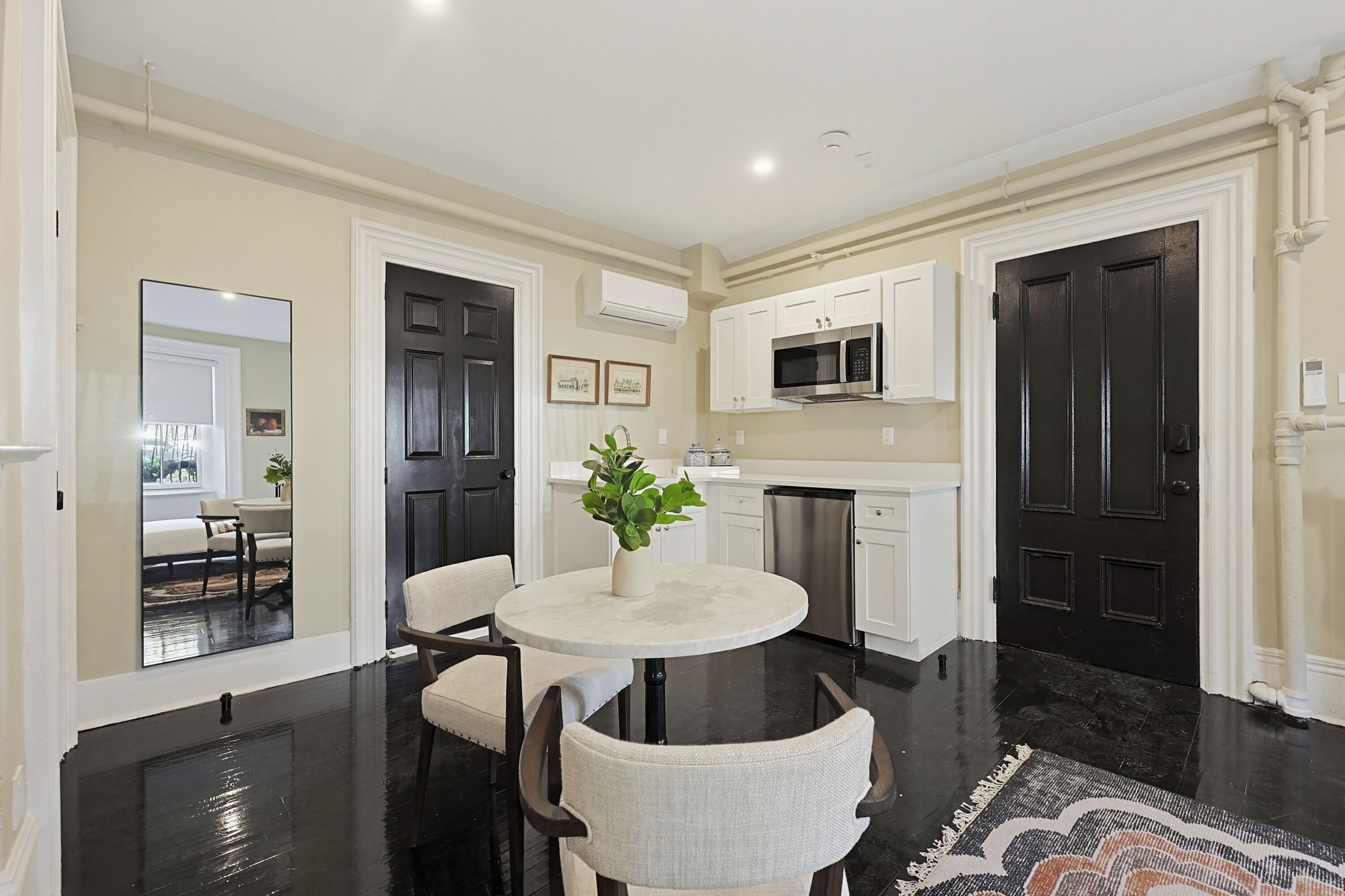 A modern kitchen with white cabinets, a black door, and a dining area with a round table and chairs.