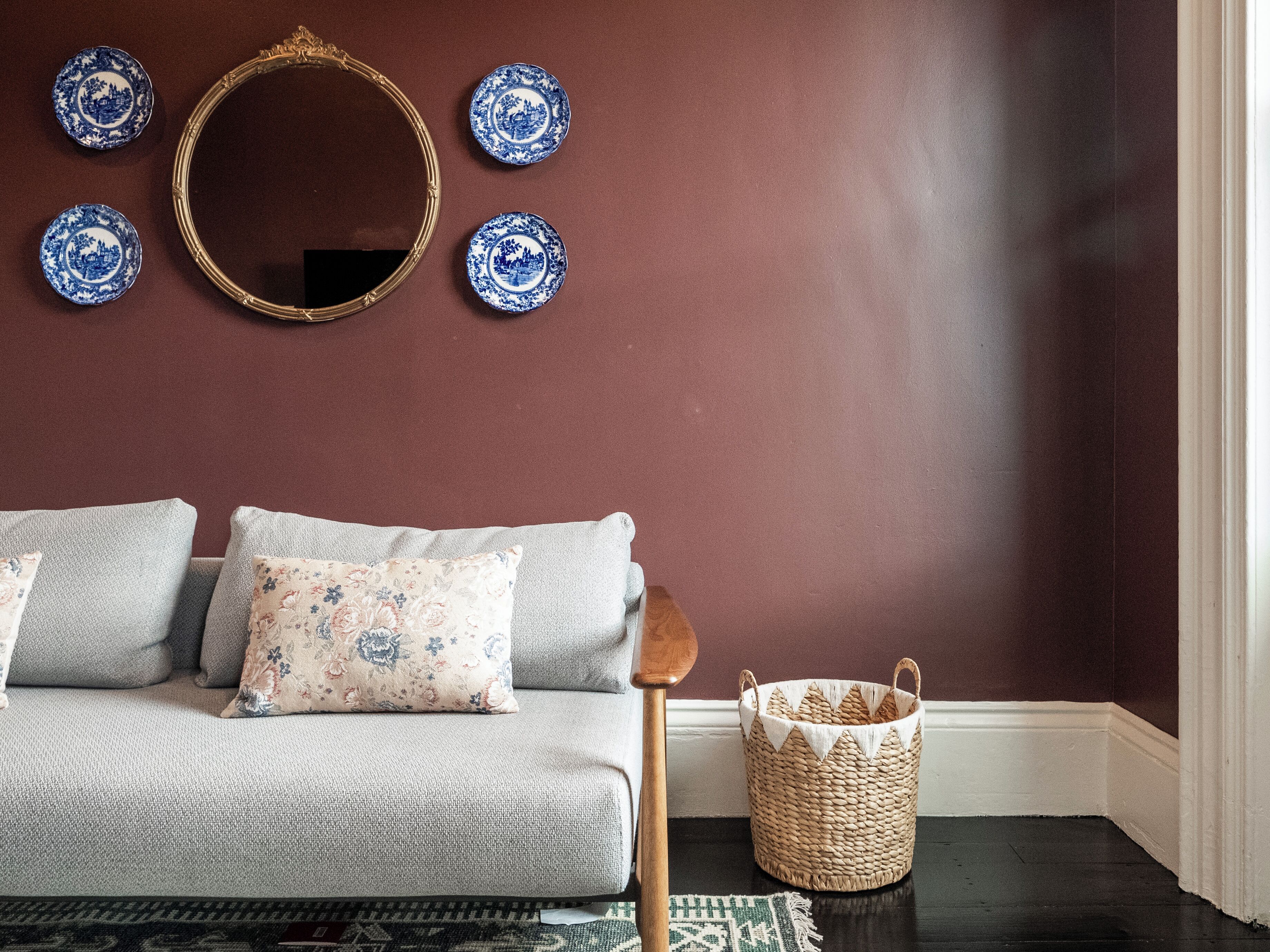 Una habitación con un sofá, almohadillas, un espejo y platos decorativos en la pared.