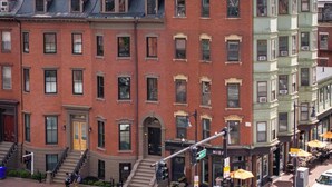Une rangée d’immeubles en briques à plusieurs étages, comprenant des logements et des commerces, dont un restaurant doté d’une terrasse.
