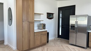 Een keuken met houten kastjes, een roestvrijstalen koelkast, een broodrooster en een spiegel aan de muur.