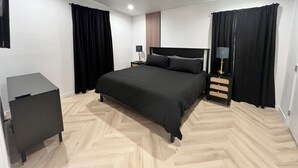 Een slaapkamer met een bed, nachtkastje met lamp, klein bureau en een kledingkast.