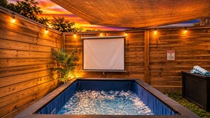 A wooden spa area with a hot tub, string lights, and a projector screen.