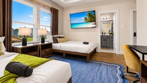 A hotel room with a bed, a desk, a chair, a TV, and a view of a beach.