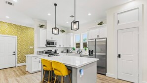 A modern kitchen with white cabinets, stainless steel appliances, and a central island with yellow bar stools.