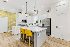A modern kitchen with white cabinets, stainless steel appliances, and a central island with yellow bar stools.