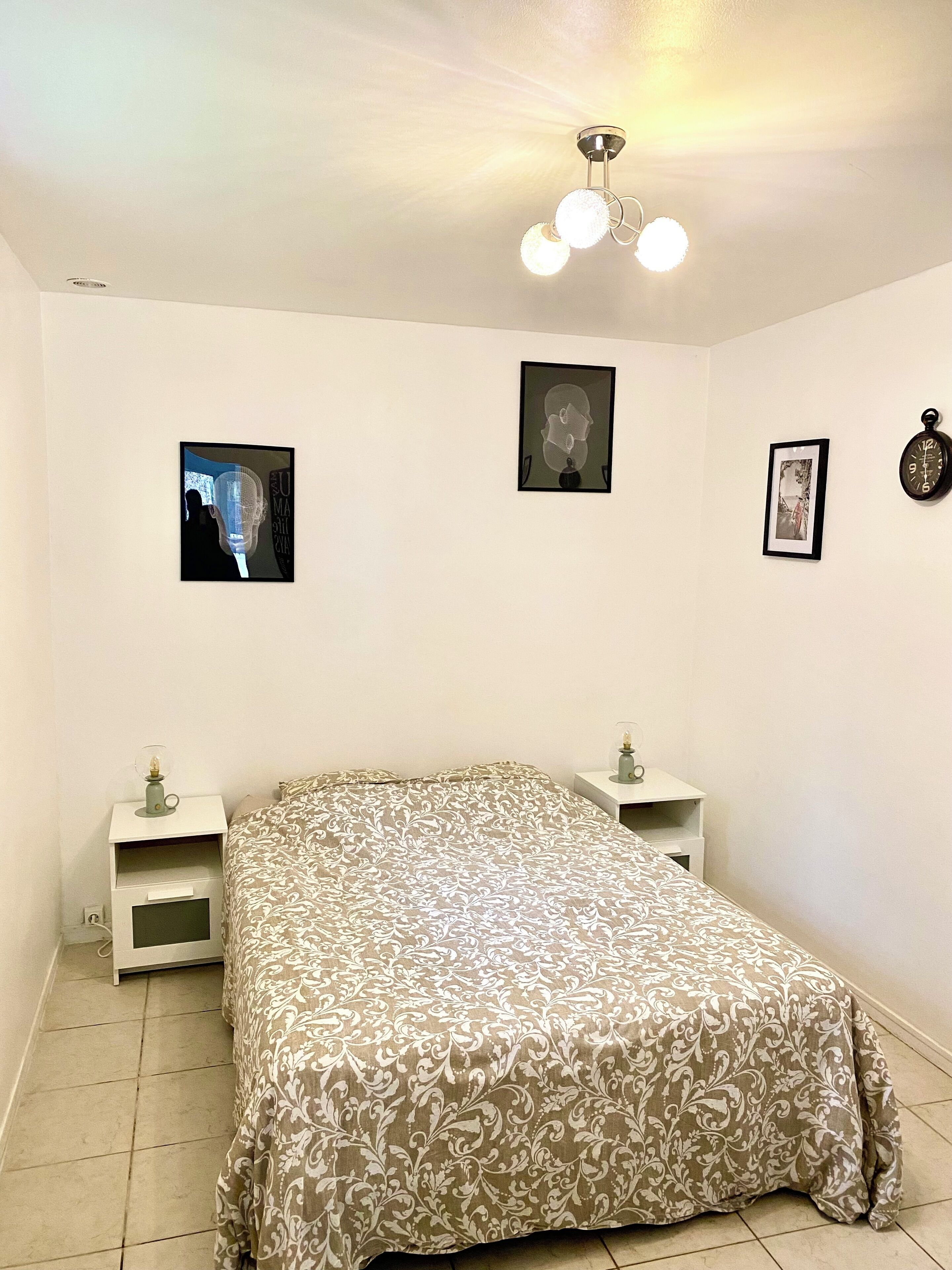 Een slaapkamer met een bed, twee nachtkastjes, een wandklok en drie ingekaderde foto’s.