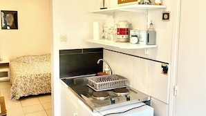 A compact kitchen with a gas stove, a small refrigerator, and a microwave. There is a bed in the adjacent room, and a sign on the wall that reads "ENJOY the little things for tomorrow you may look back and realize they were the BIG THINGS." - Charmant Studio à Coutevroult (Coutevroult)