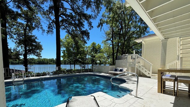 A swimming pool with clear blue water, surrounded by trees and a view of a lake. -  The Hap Haven- a Charming Lakefront Retreat in East Texas - Perfect Getaway! (Lone Star)