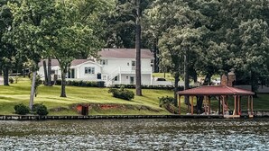 A lakeside property with a white house, a gazebo, and dense trees. -  The Hap Haven- a Charming Lakefront Retreat in East Texas - Perfect Getaway! (Lone Star)