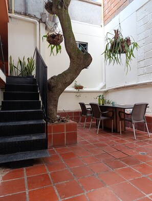 A patio area with a staircase, a dining table with chairs, and hanging plants. - Casa Primavera Hostal (Medellín)