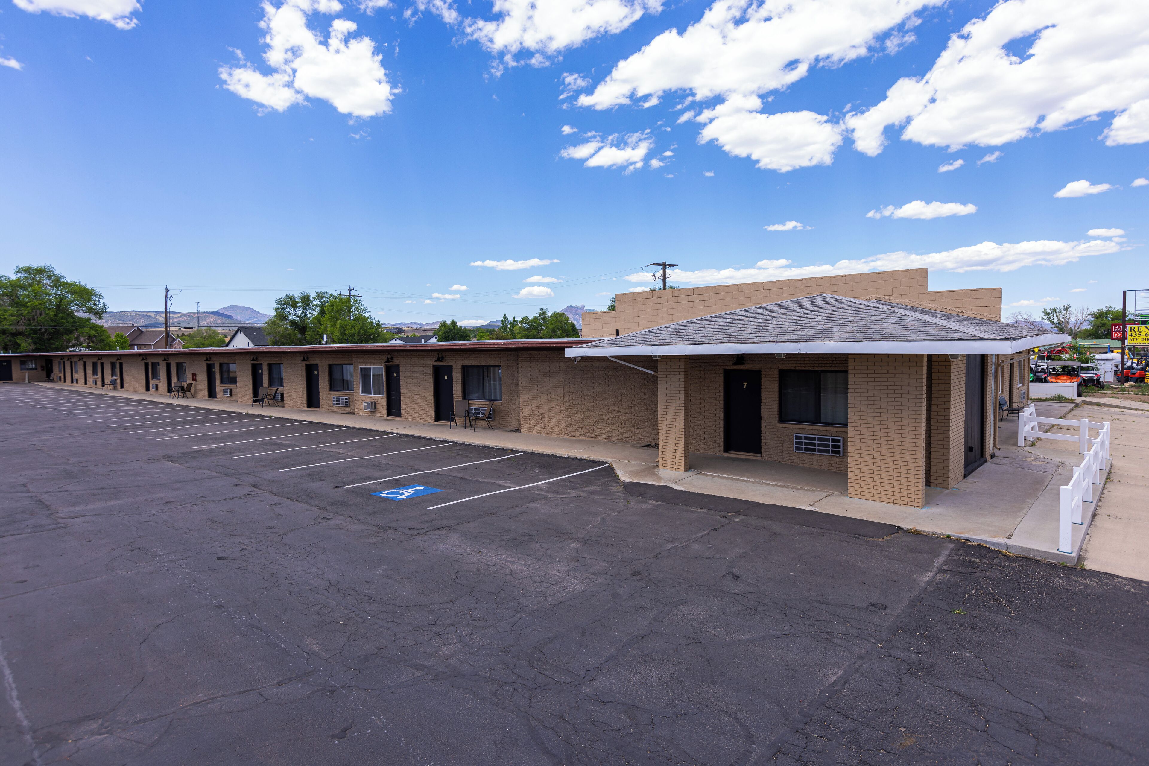 A motel with a parking lot, a small building with a flat roof, and a clear blue sky with clouds.