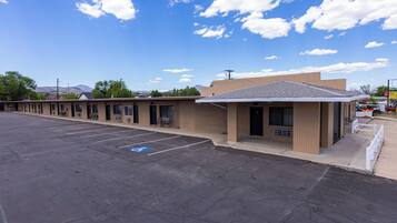 A motel with a parking lot, a small building with a flat roof, and a clear blue sky with clouds.