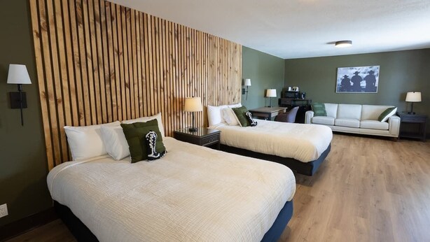 A hotel room with two beds, a wooden headboard, a green wall, a sofa, and a painting. - The Golden Spurs (Panguitch)