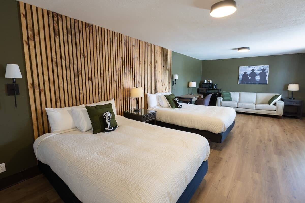 A hotel room with two beds, a wooden headboard, a green wall, a sofa, and a painting.