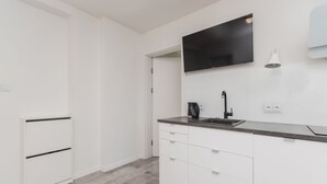 Eine moderne Küche mit weißen Schränken, einer schwarzen Arbeitsplatte, einer eingebauten Spüle und einem flachbildfernseher, der über der Arbeitsfläche angebracht ist.