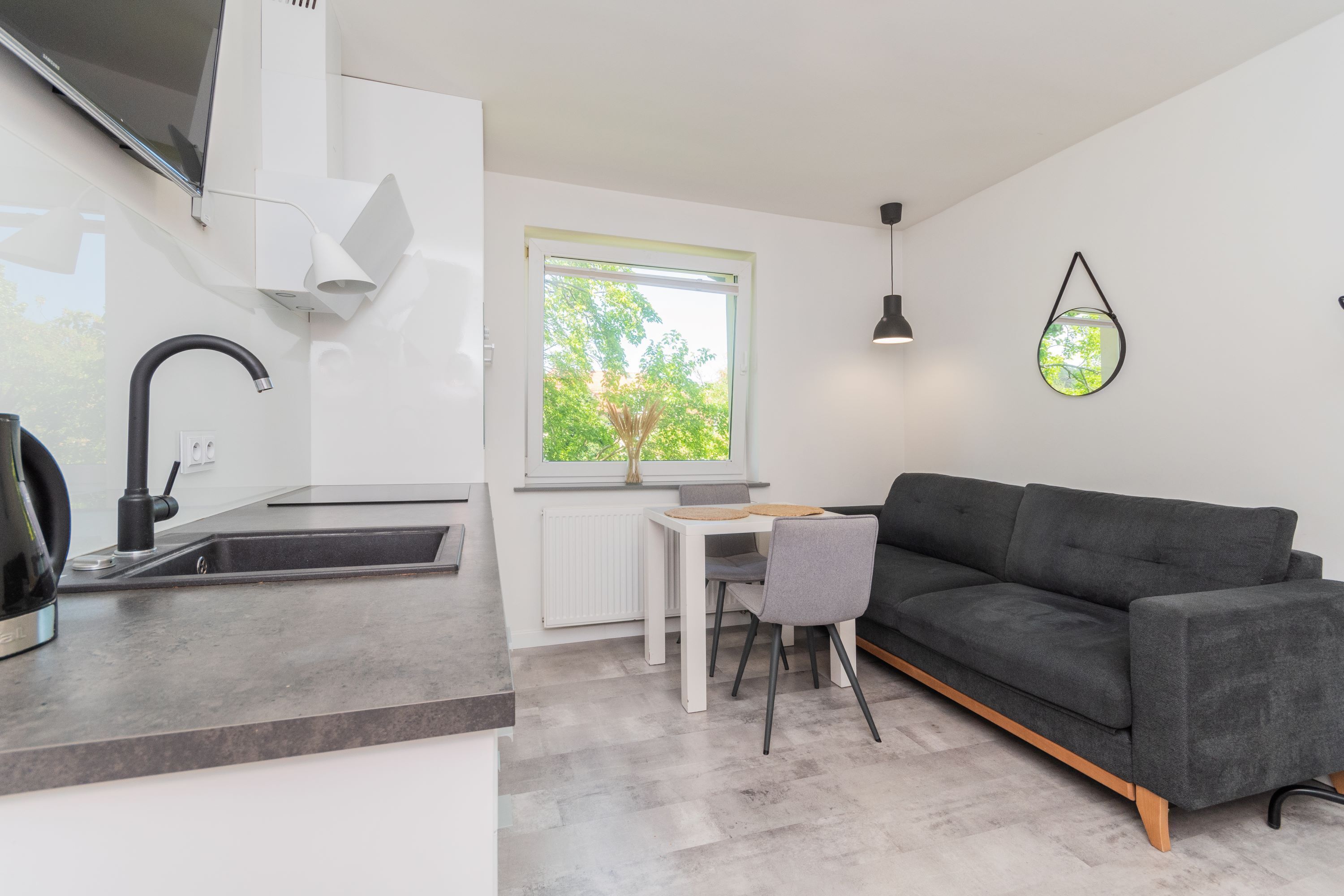 A modern kitchen with a built-in stove, a dining area with a table and chairs, and a dark grey sofa.