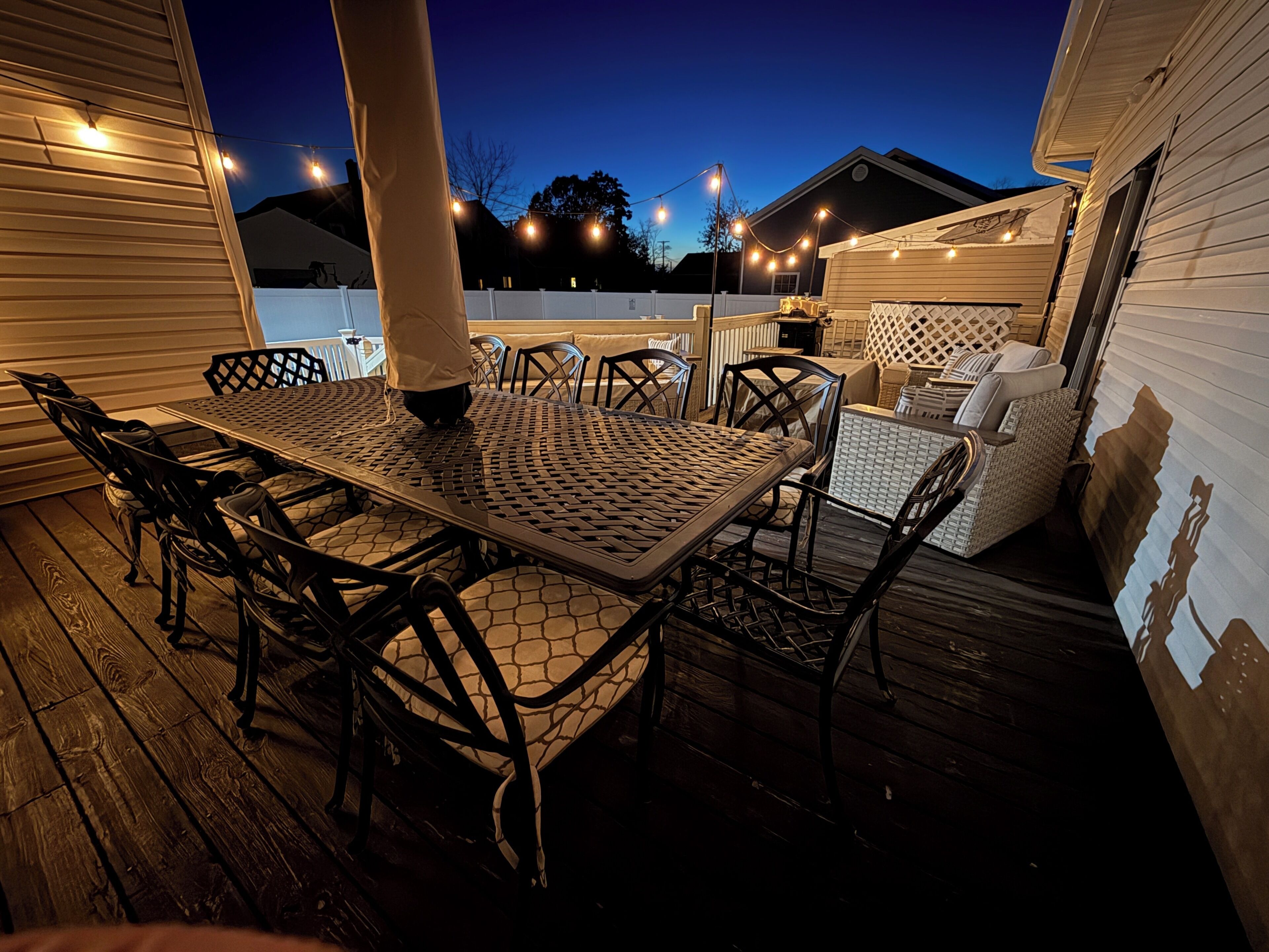 An outdoor patio with a metal table and chairs, surrounded by a wooden deck.