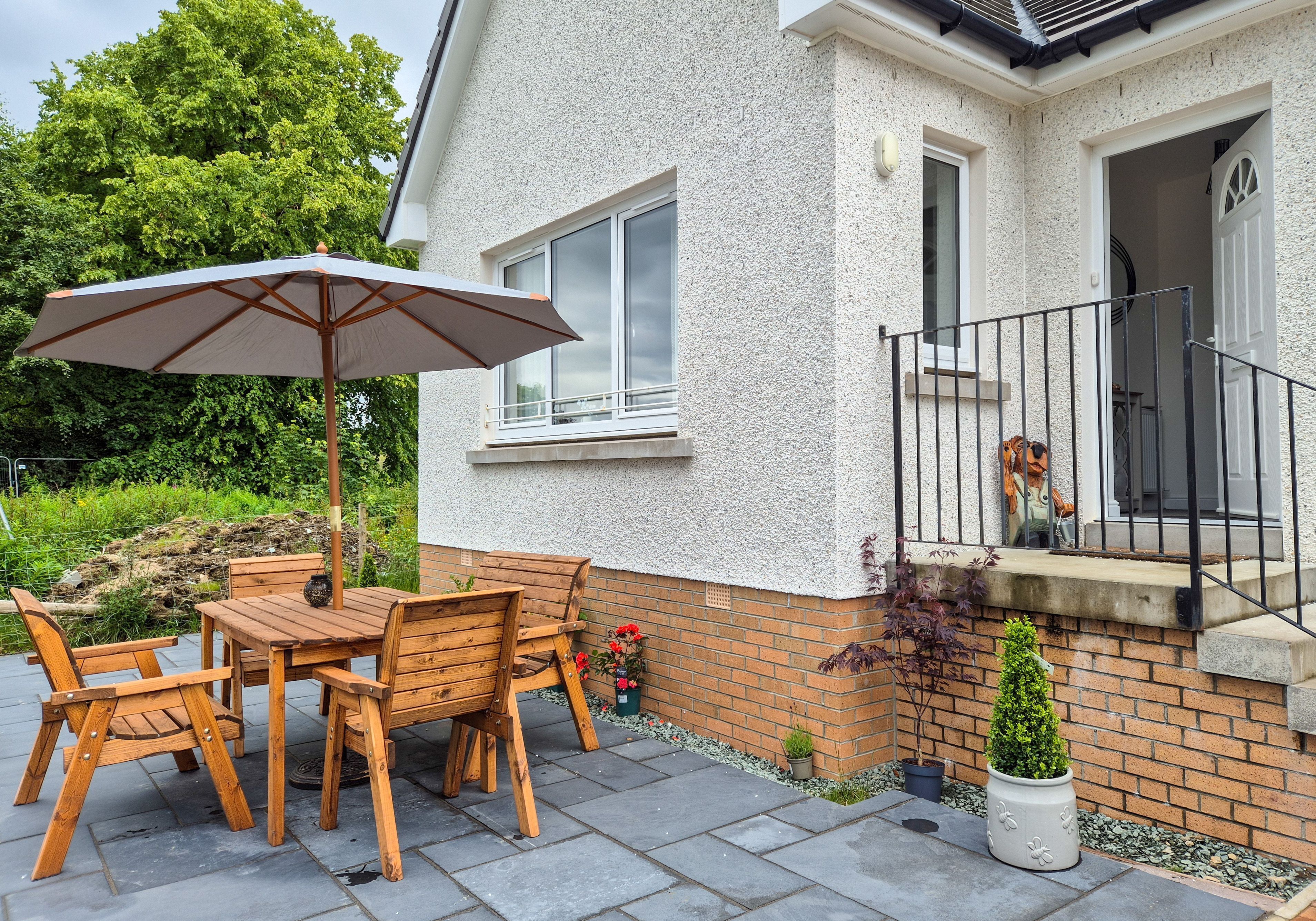 A patio with a wooden table and chairs, a large umbrella, and a potted plant.