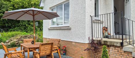 A patio with a wooden table and chairs, a large umbrella, and a potted plant.