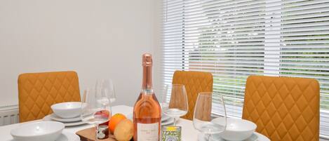 A dining table set with white plates, bowls, and glasses, a bottle of wine, and a wooden board with fruits and a candle.