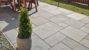 Un patio con una mesa y sillas de madera, una planta en maceta y una cerca de madera al fondo.