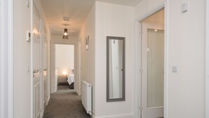 Un pasillo con paredes blancas, un radiador, un espejo y una puerta que da a otra habitación.