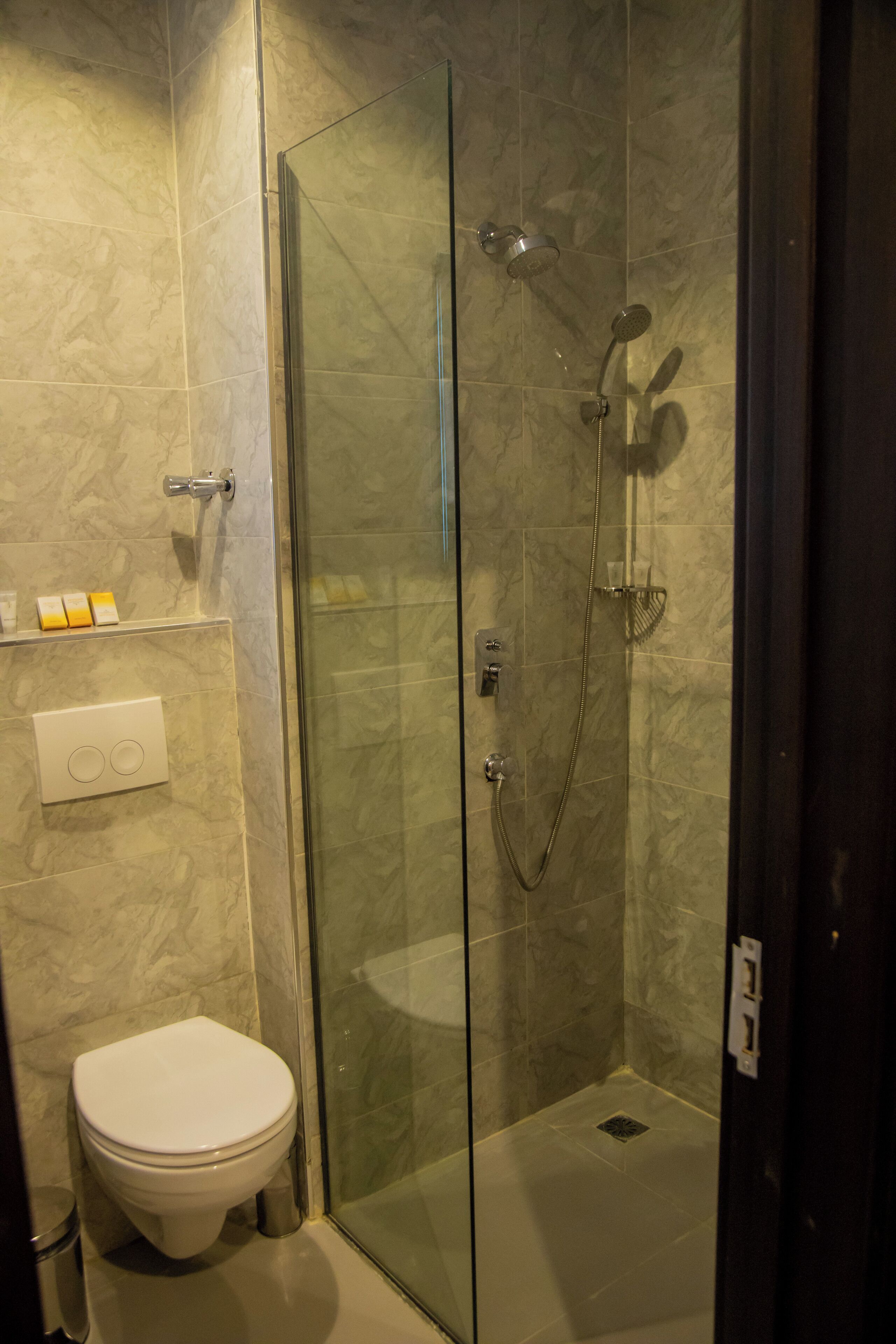 A glass-enclosed shower with a handheld showerhead and a wall-mounted faucet.