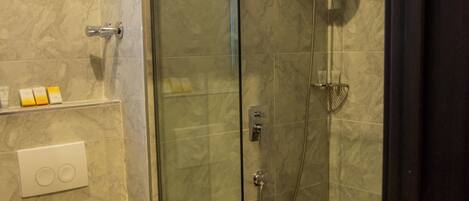 A glass-enclosed shower with a handheld showerhead and a wall-mounted faucet.