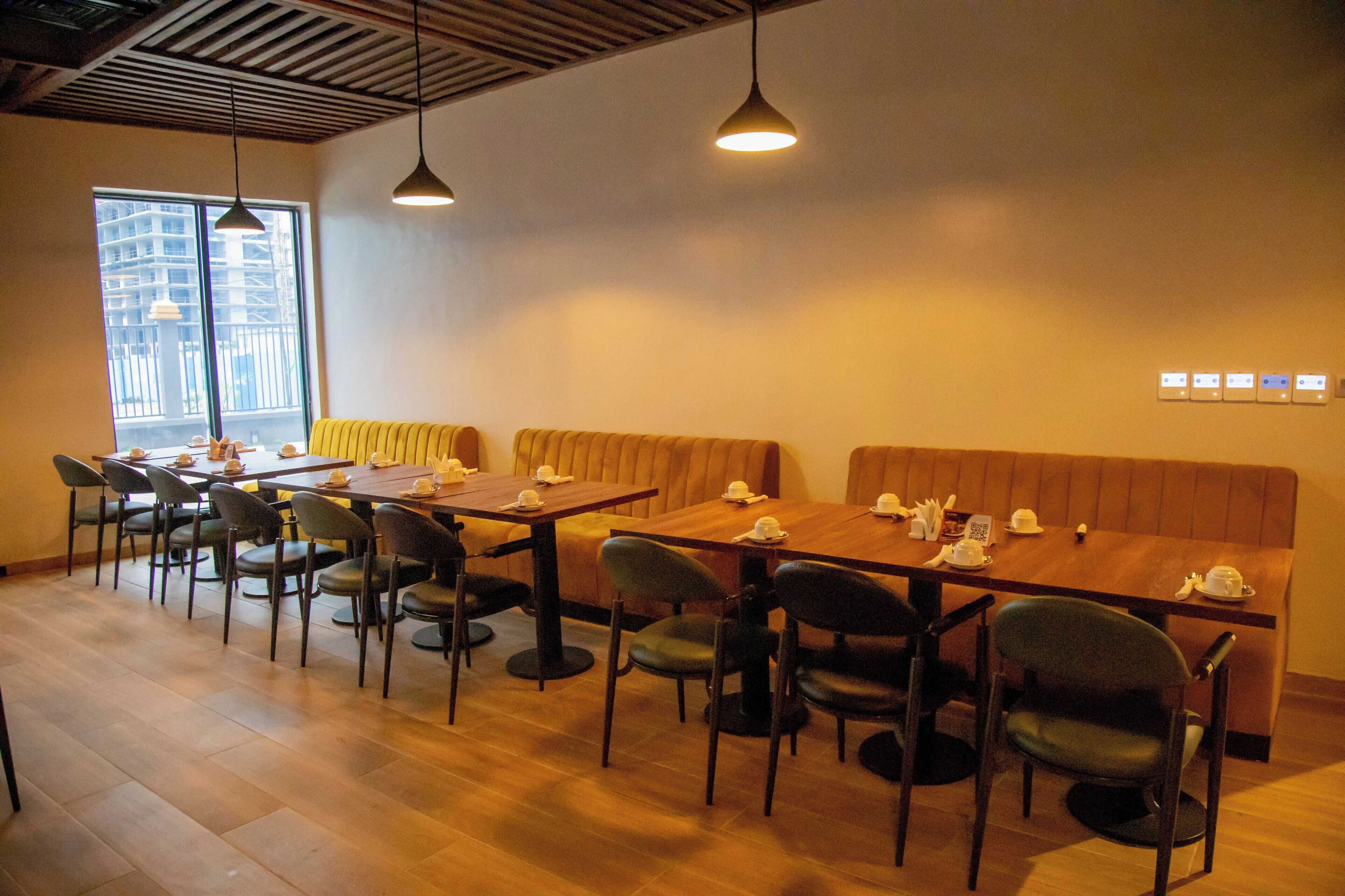 A restaurant with wooden tables and chairs, a high ceiling with exposed beams, and large windows offering a view of the city.