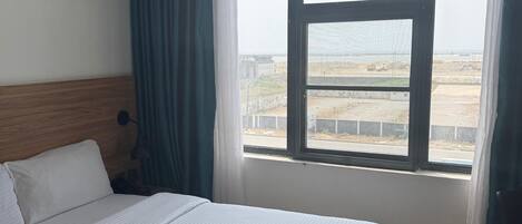 Habitación de hotel con una cama grande, cabecera de madera, ventana con cortinas y vistas al exterior.