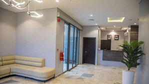 A modern lobby with a beige sectional sofa, a reception desk, a potted plant, and a fire extinguisher. - Hotelinn Oniru  (Lagos)