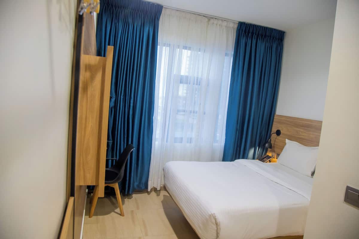 A hotel room with a bed, a desk with a chair, and curtains.