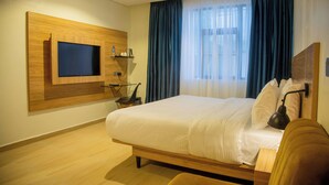 A modern hotel room with a large bed, a mounted TV, and a bedside table with a lamp. - Hotelinn Oniru  (Lagos)