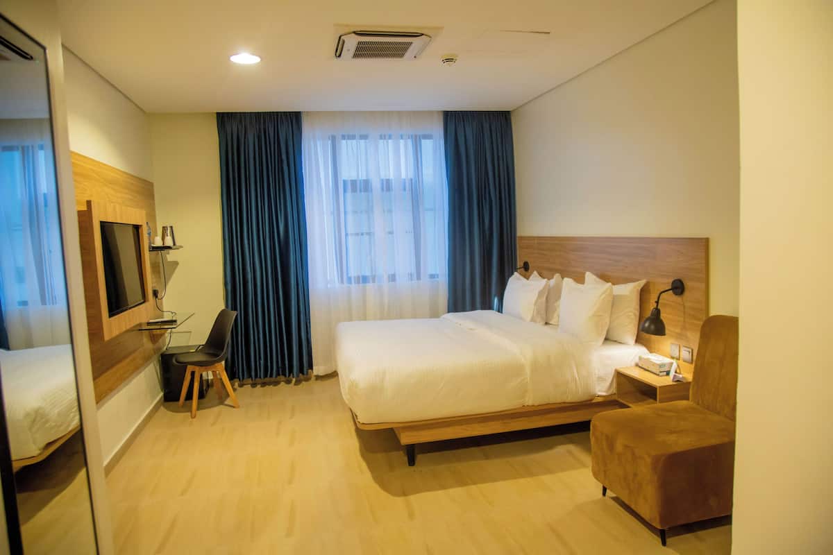 A hotel room with a large bed, a desk with a chair, a TV, and a window with curtains.