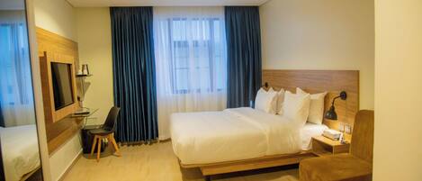 A hotel room with a large bed, a desk with a chair, a TV, and a window with curtains.