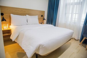 Una cama bien hecha con sábanas blancas, cabecera de madera y dos lámparas de noche.