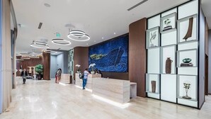Een moderne hotellobby met een receptiebalie, een groot abstract schilderij en een presentatie van decoratieve objecten.