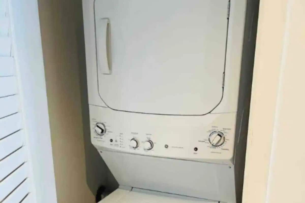 Een kleine, witte wasruimte met een verticaal gestapelde wasmachine en droger.