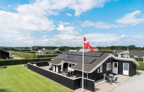 A modern building with solar panels, a flag, and a patio area with tables and chairs.