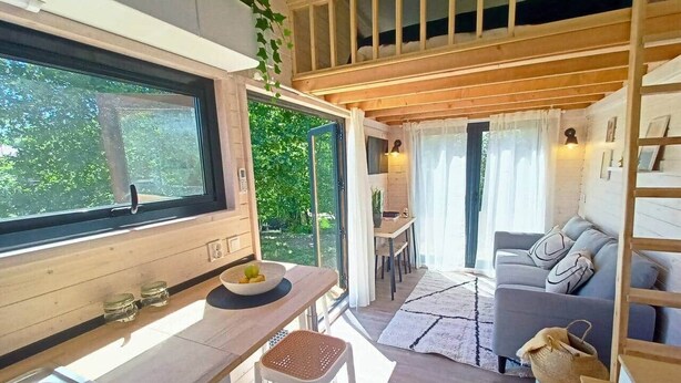 A compact kitchen with a large window, a dining area with a table and chairs, and a sofa in a living space.