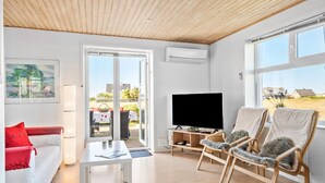 A modern living room with a white sofa, a red pillow, a coffee table, a TV, and two wicker chairs. - 4 bedroom nice home in Harboøre (Harboøre)